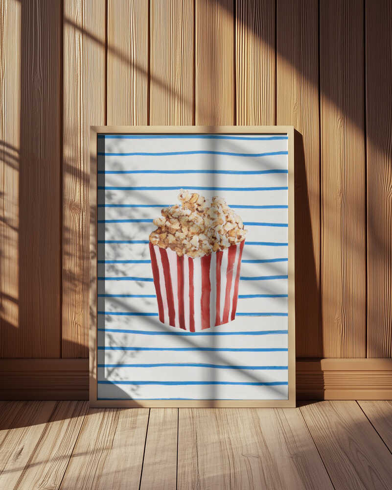 Inramad barntavla med popcornmotiv ståendes på golvet i barnrum med träpanel på väggen. En varm och harmonisk inredningsstil.
