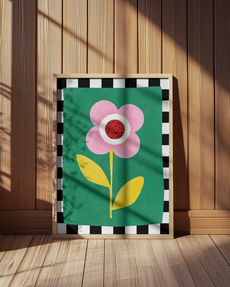 Inramad barnrumstavla med rosa blomma och gula blad, placerad på golvet framför träpanel. En varm och lekfull inredningsdetalj.
