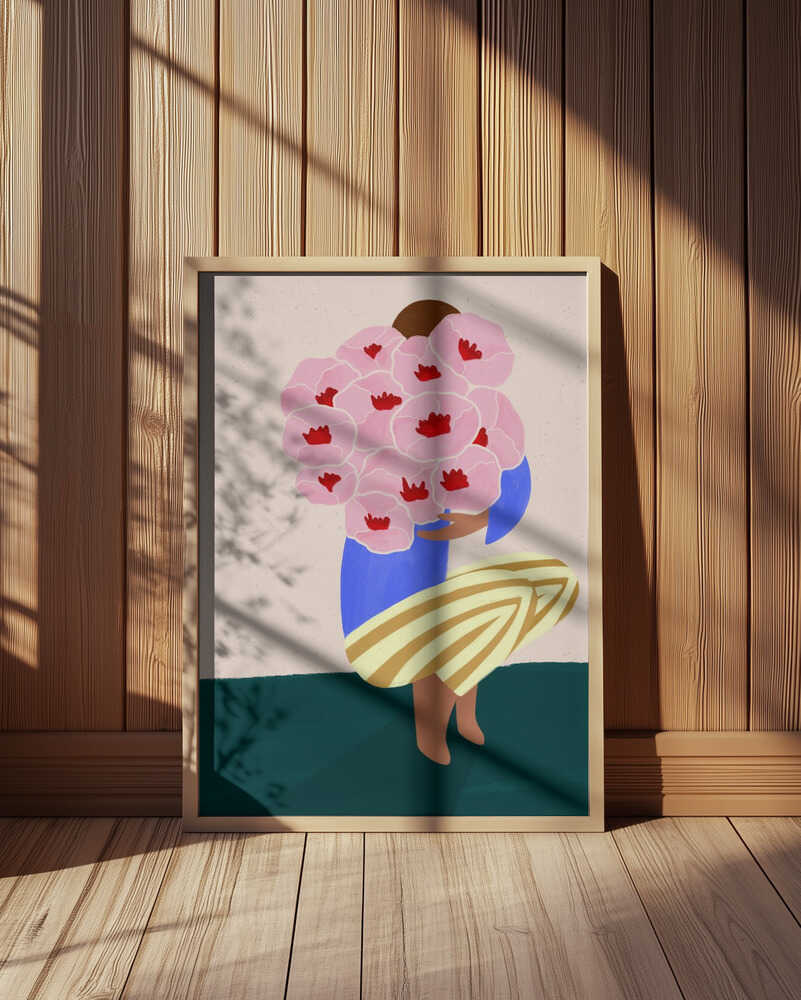 Inramad barnrumstavla med rosa blommor och person i blått och gult, placerad på golvet framför träpanel. En varm och konstnärlig detalj.