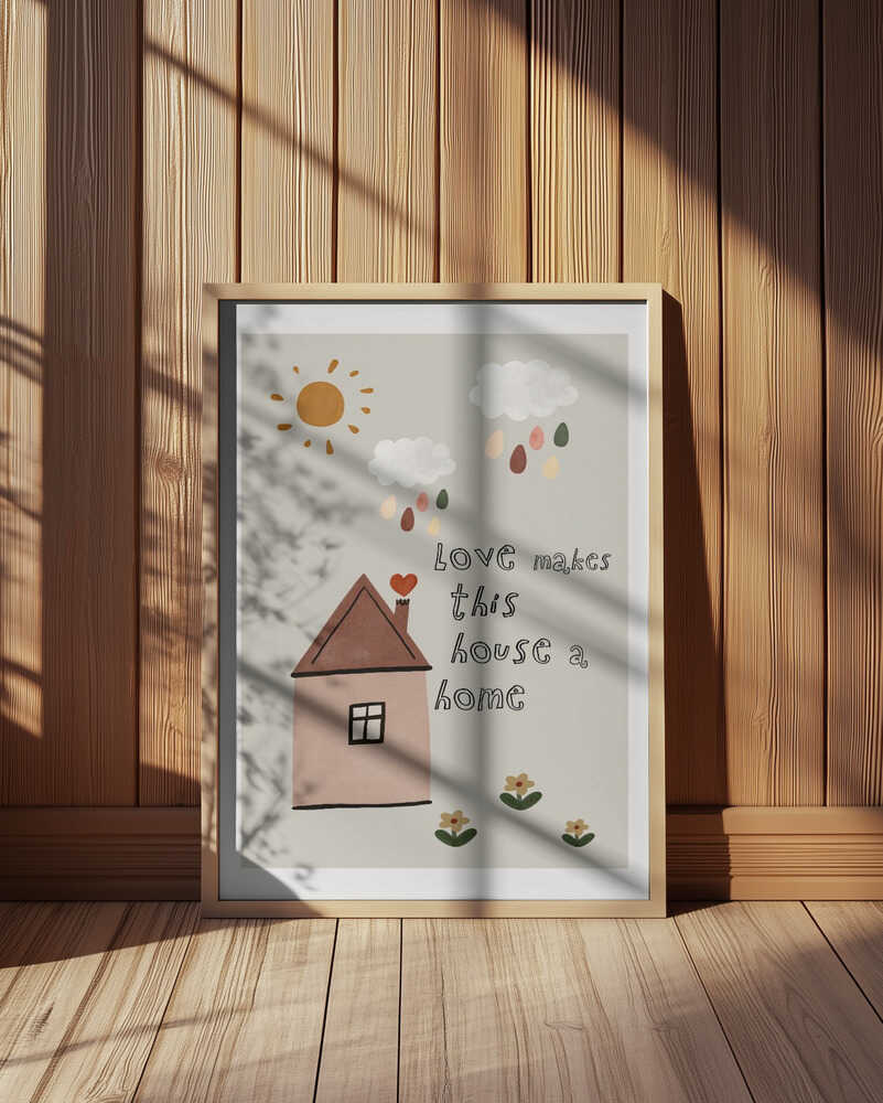 Inramad barntavla med illustrerat hus, placerad framför träpanel. Texten “love makes this house a home” ger rummet en varm, sagolik karaktär.