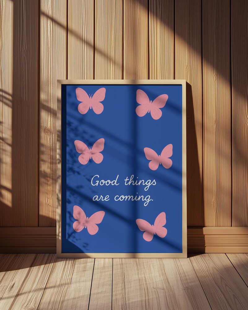 Inramad barntavla med fjärilar och texten "GOOD THINGS ARE COMING" placerad på golvet framför träpanel för en varm känsla.