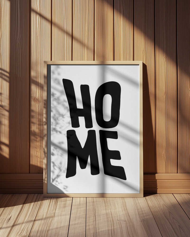 Barntavla med texten "HOME" i svart på vit bakgrund, inramad i träram och placerad mot en vägg med träpanel. Solens skuggspel skapar en varm och harmonisk känsla som lyfter tavlans enkla uttryck.