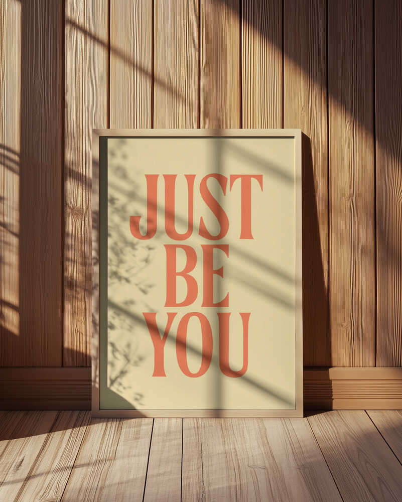 Inramad barnrumstavla med "JUST BE YOU" på gul bakgrund, placerad på golvet framför en träpanel. En varm och harmonisk miljö.