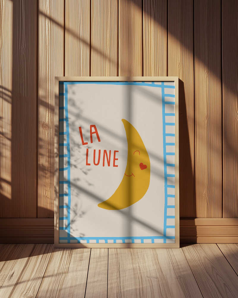 Inramad barntavla med “LA LUNE” placerad på golvet framför träpanel som förstärker det varma uttrycket.