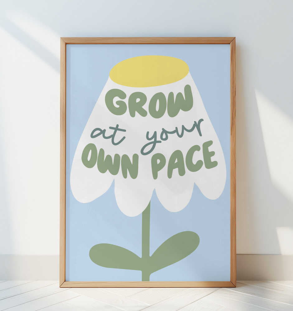 Barntavla med blomma och texten "GROW AT YOUR OWN PACE" i ram, lutad mot en vit vägg i barnrum. En stilren och mjuk inredningsdetalj.