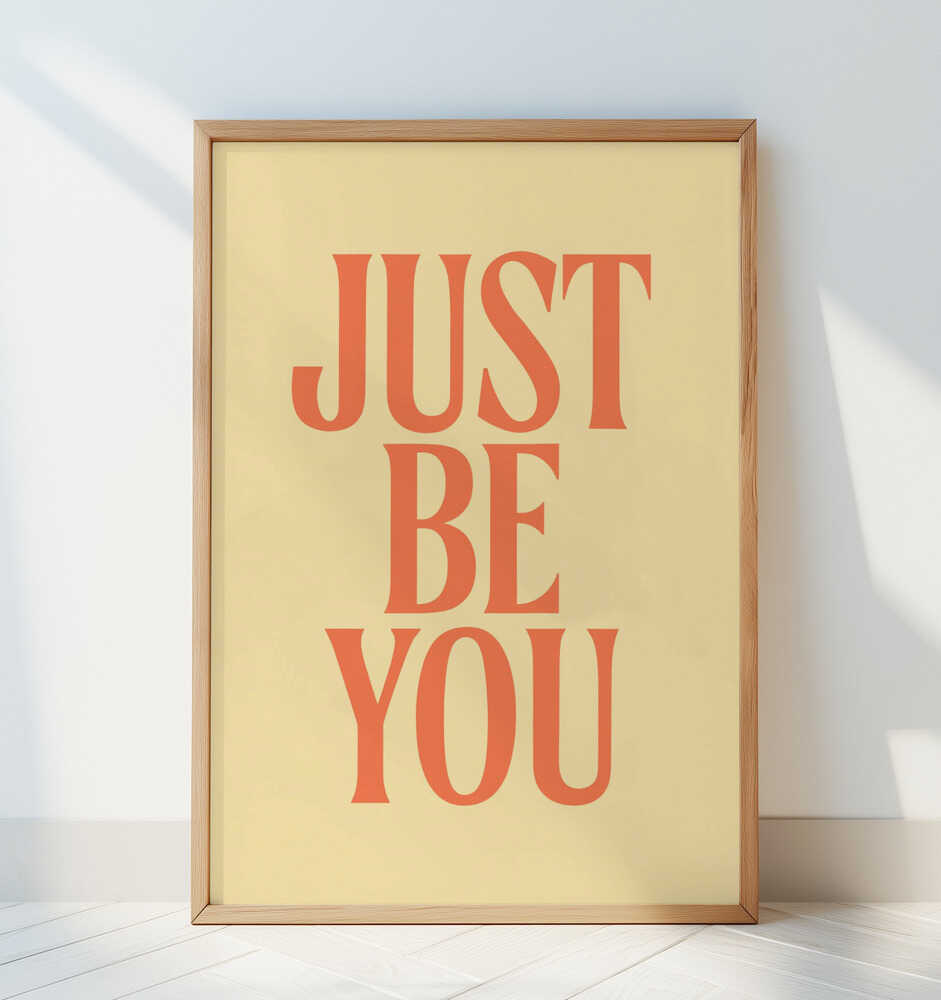 Inramad barnrumstavla med texten "JUST BE YOU", lutad mot vit vägg i ett minimalistiskt rum. En mjuk och positiv färgaccent.