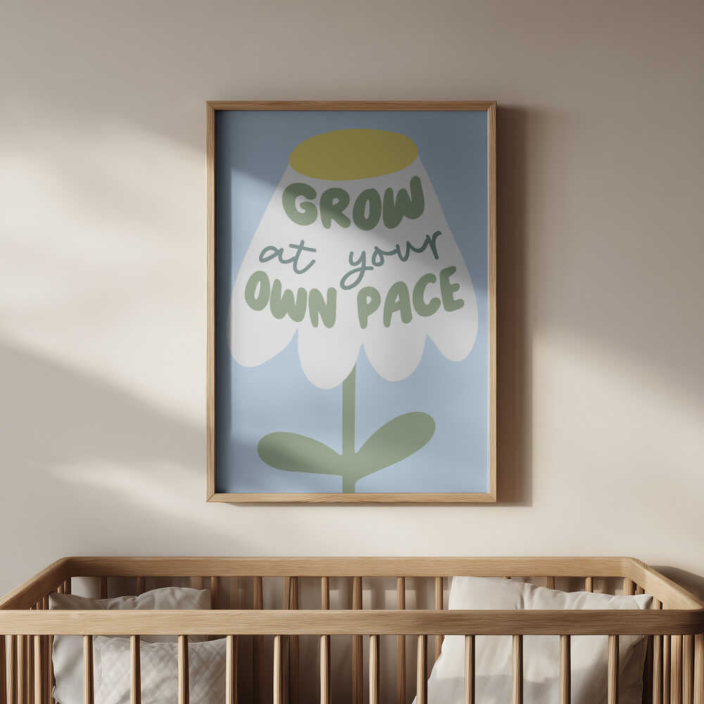 Barntavla med vit blomma och texten "GROW AT YOUR OWN PACE" i ram, placerad ovanför spjälsängen i barnrum. En lugn och trygg dekoration för barnets första rum.